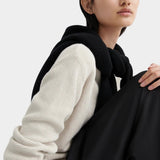 Close-up of model wearing a cream waffle-knit crewneck sweater with a black sweater draped over shoulders.