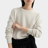 Model standing in a cream textured knit sweater with ribbed cuffs, styled with a black midi skirt.