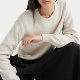 Model seated wearing a textured cream crewneck sweater with black midi skirt and black leather shoes.