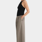 Side view of the cropped black Kowtow Low Back Cami styled with taupe trousers.