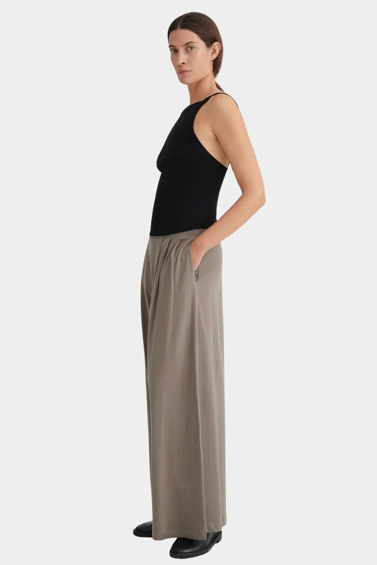 Side view of the cropped black Kowtow Low Back Cami styled with taupe trousers.