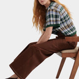 Kowtow Unity Jeans in brown denim worn with plaid knit top, seated side view