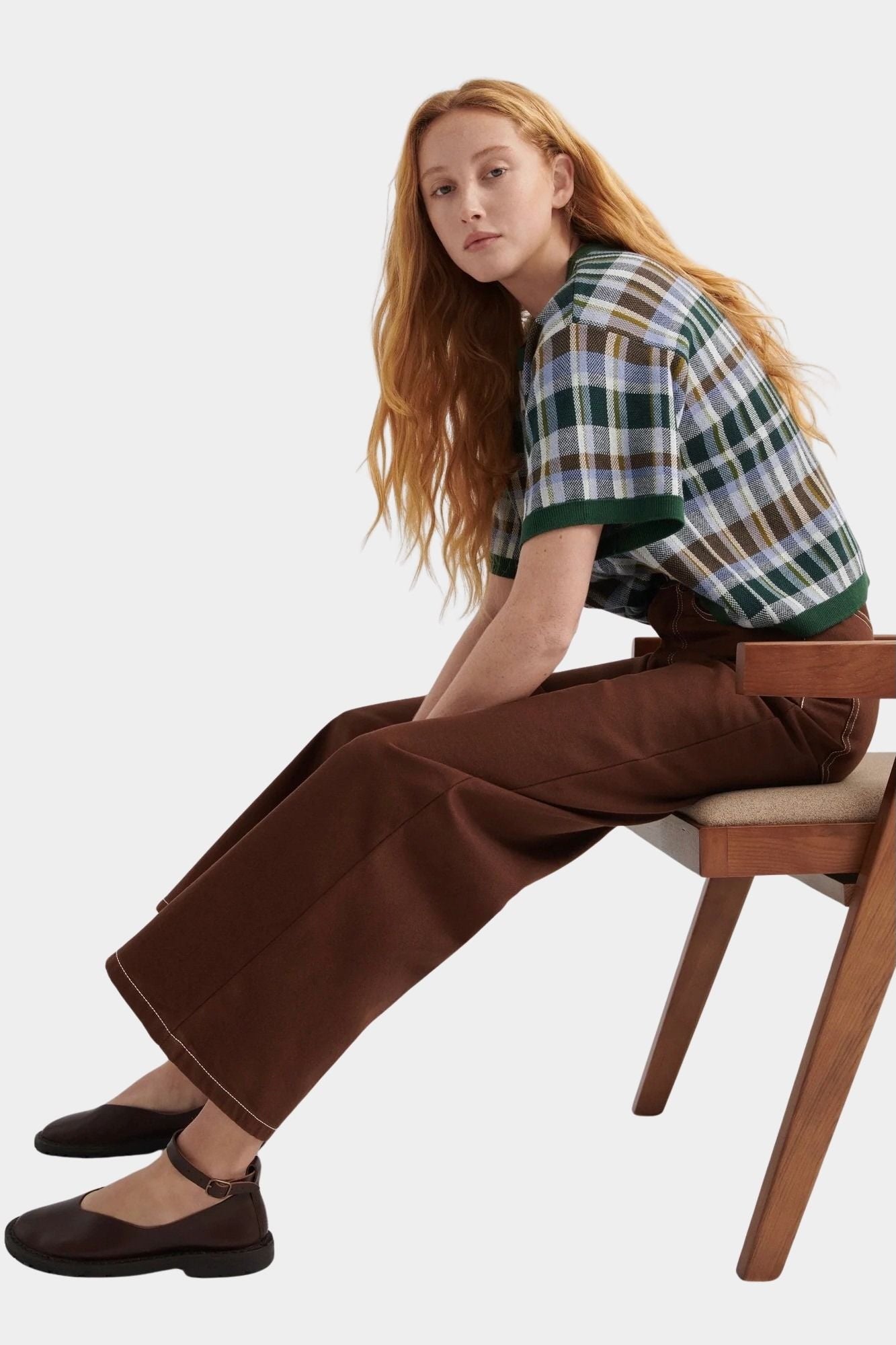 Kowtow Unity Jeans in brown denim worn with plaid knit top, seated side view