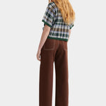 Kowtow Unity Jeans in brown denim worn with plaid knit top, full length back view