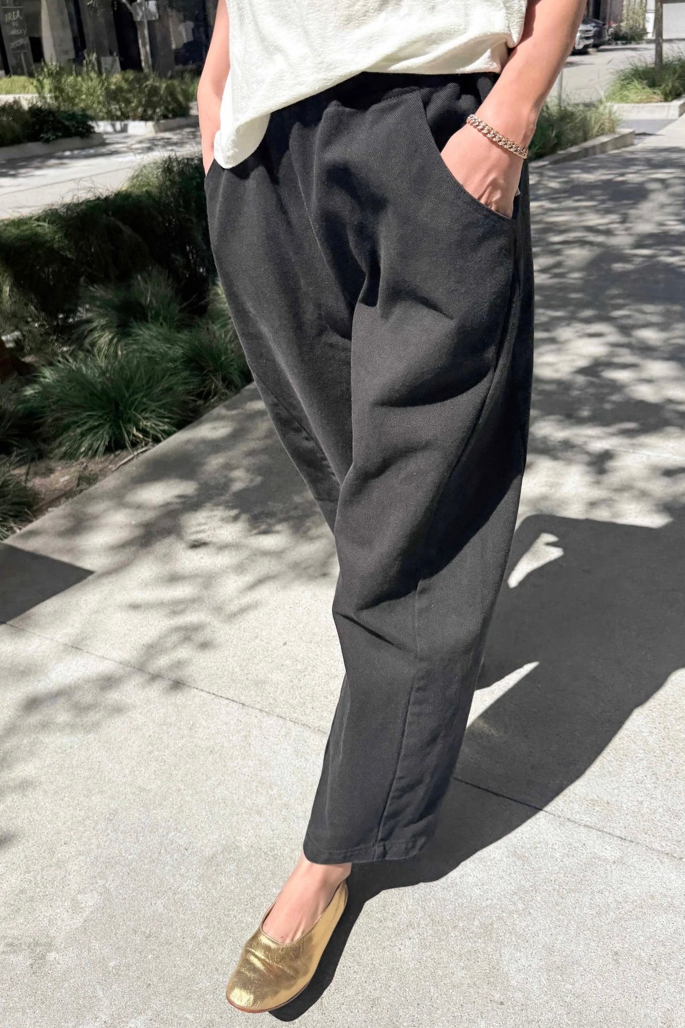 Black canvas Arc Pants styled with a white tee and gold flats, featuring oversized pockets and a relaxed tapered leg.