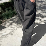 Front view of black canvas Arc Pants styled with a white tee and gold flats, highlighting the relaxed fit and curved silhouette.