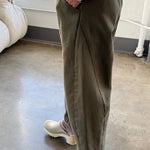 Side view of olive Arc Pants styled with a cream knit sweater and ivory clogs, highlighting the relaxed fit and curved leg silhouette.