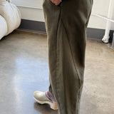 Side view of olive Arc Pants styled with a cream knit sweater and ivory clogs, highlighting the relaxed fit and curved leg silhouette.