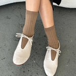 Dark Tan ribbed cotton socks styled with ivory lace-up ballet flats and a black skirt on concrete flooring