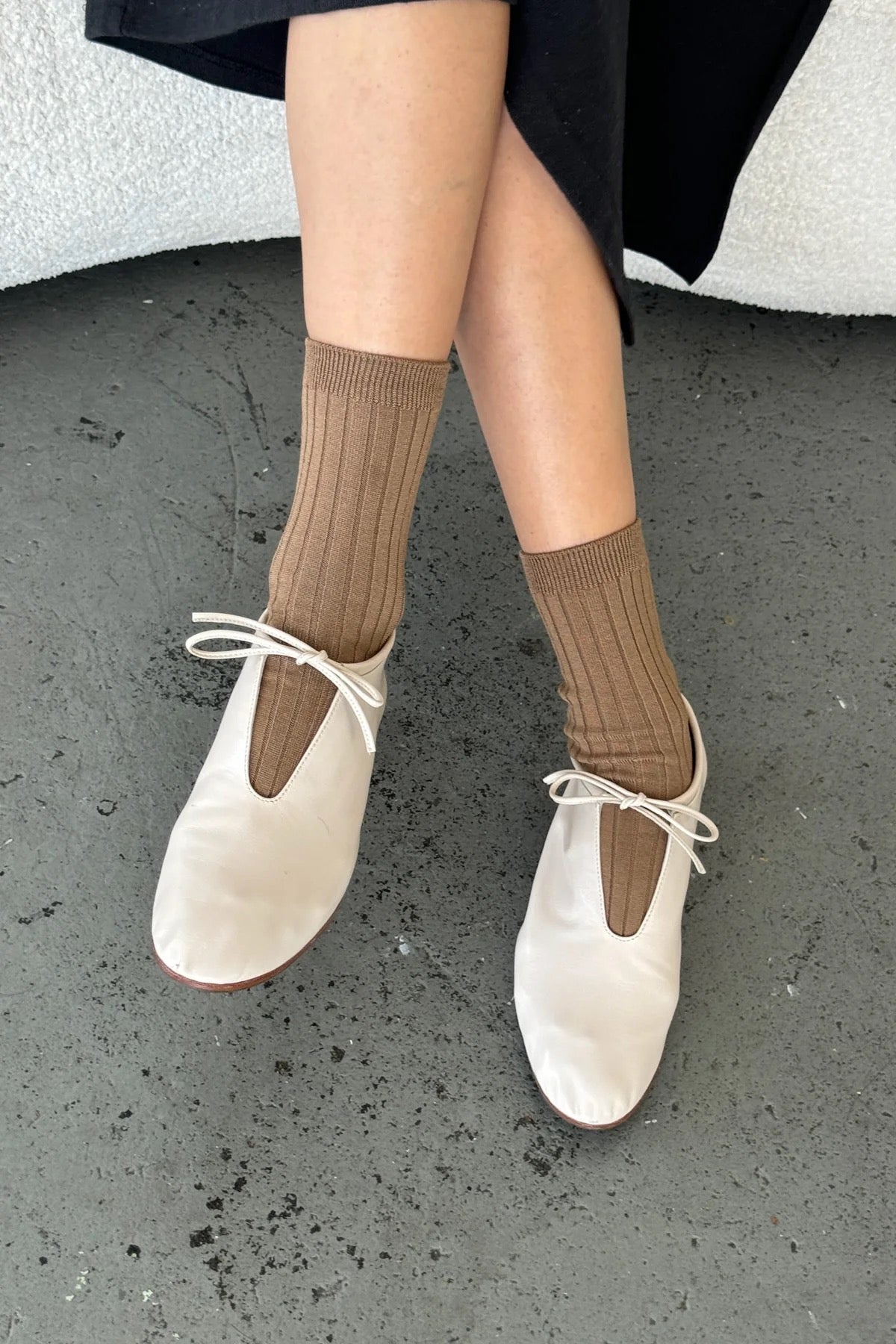 Dark Tan ribbed cotton socks styled with ivory lace-up ballet flats and a black skirt on concrete flooring