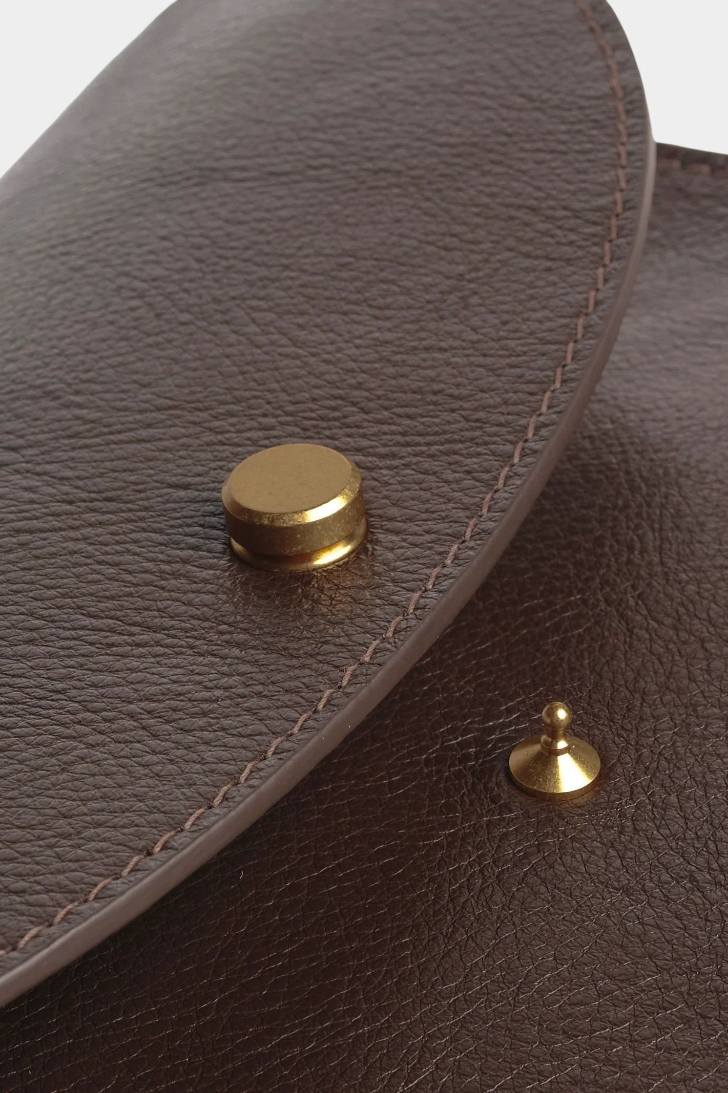 Close view of the Chaga Mezzo bag’s brass flap closure, pebbled leather, and tonal stitching