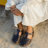 LOQ Rio sandal in black worn on sand with light dress showing flat leather fisherman sandal and ankle strap