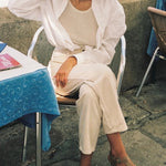 LOQ Rio sandal in taupe worn with cream outfit seated outdoor showing flat leather fisherman sandal and ankle strap