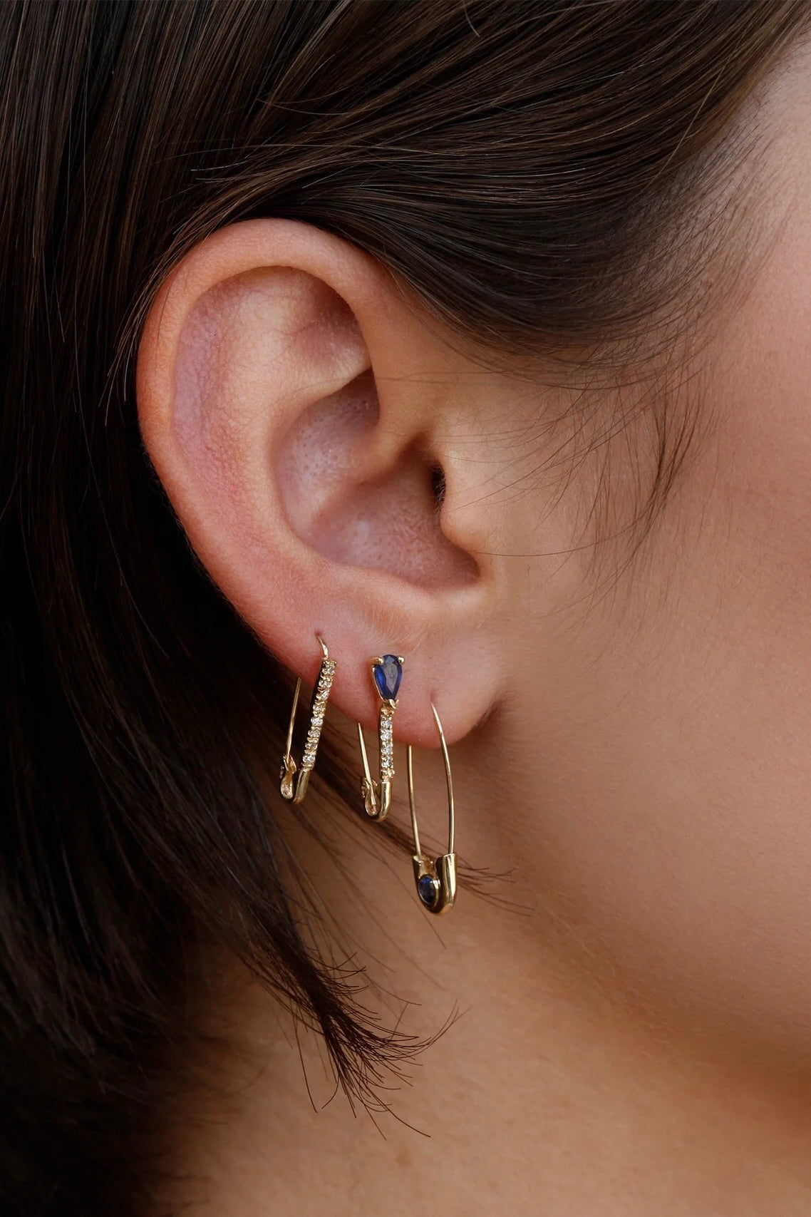 Loren Stewart Cirque Safety Pin Earring with blue sapphire worn in a layered gold ear stack