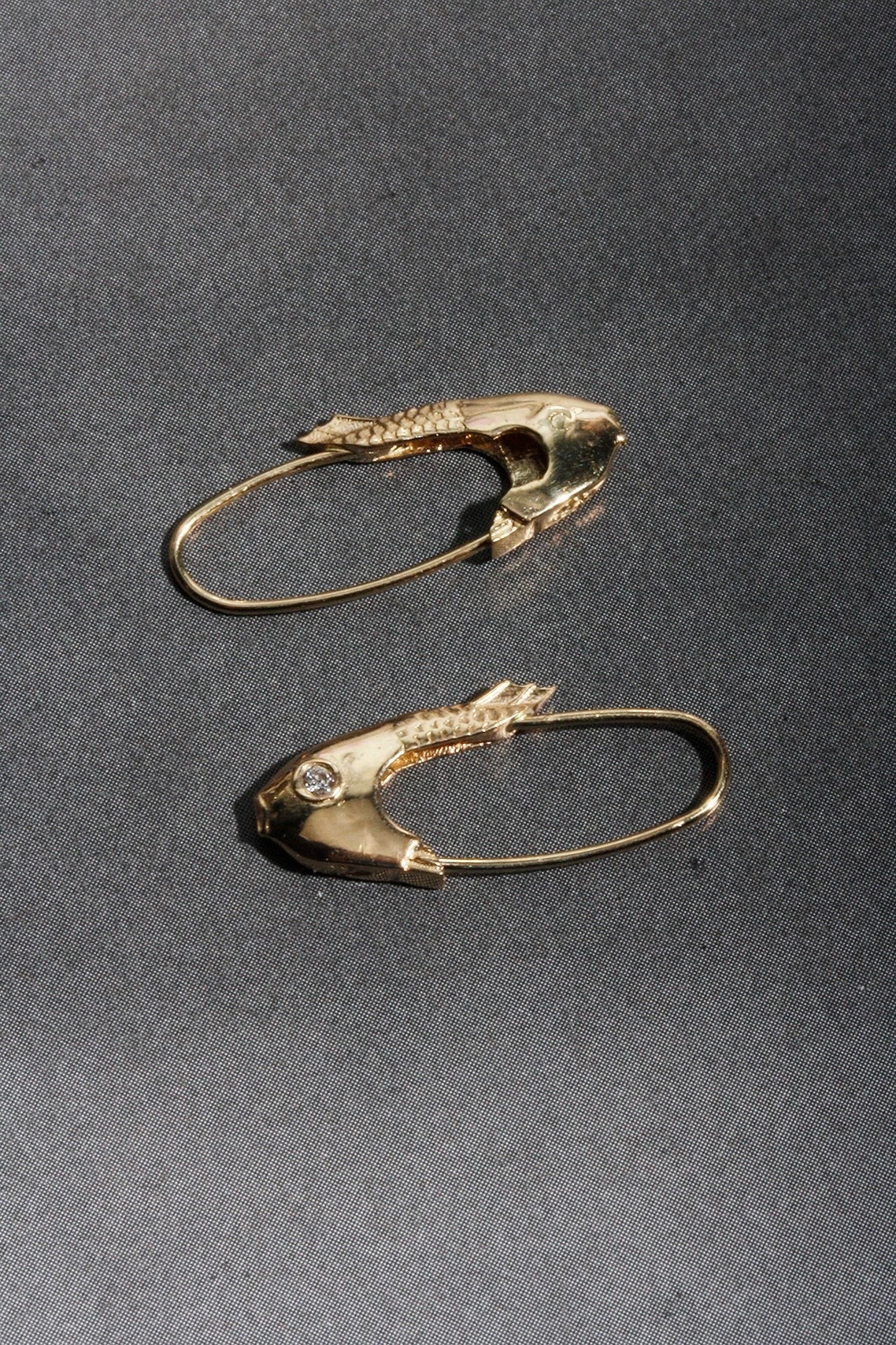 Mirrored Pisces fish earrings in 14k yellow gold displayed on gray fabric