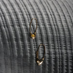 Two 14k yellow gold Pisces Safety Pin Earrings photographed on dark textured fabric