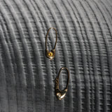 Two 14k yellow gold Pisces Safety Pin Earrings photographed on dark textured fabric