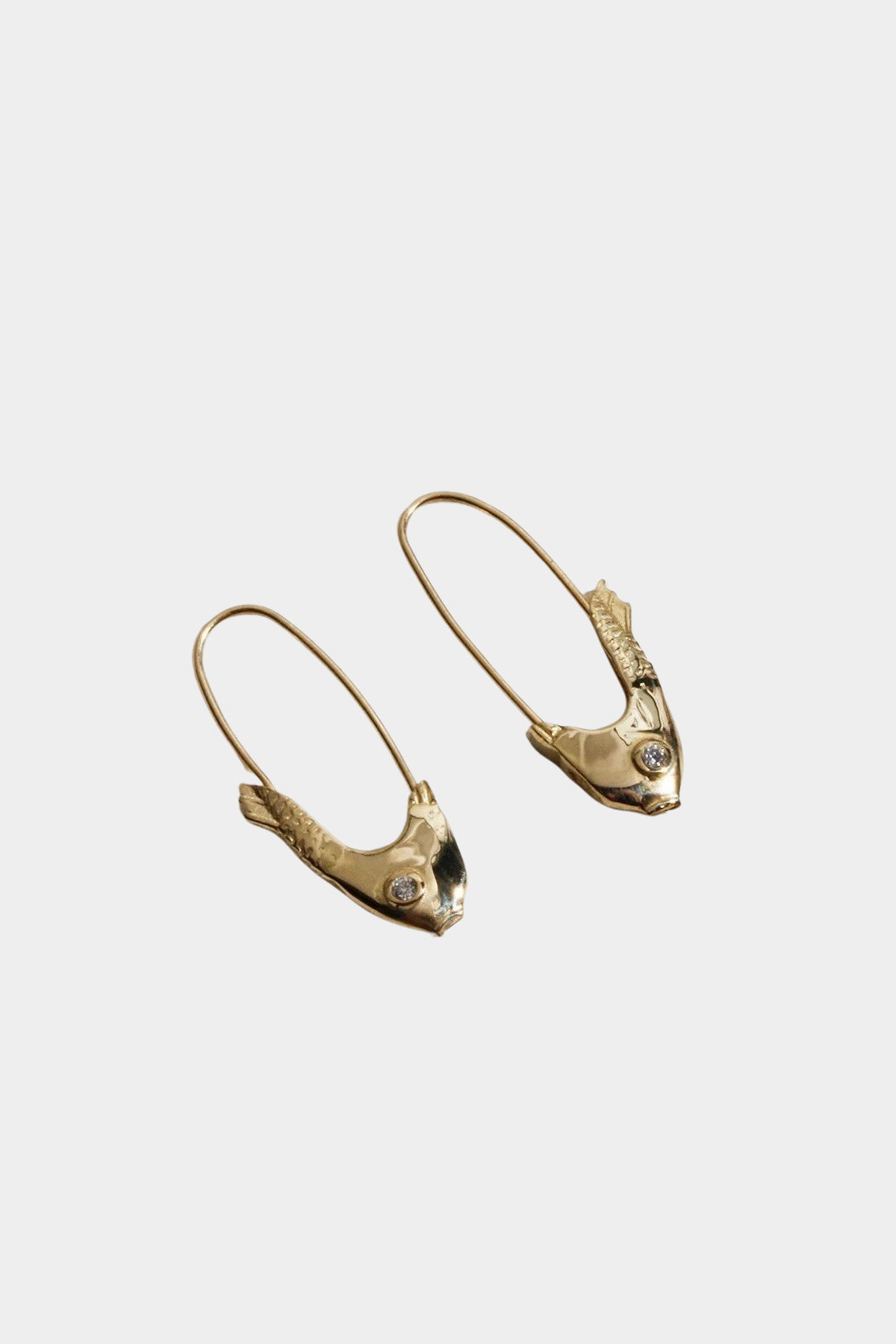 Mirrored Pisces fish earrings in 14k yellow gold displayed on gray fabric