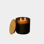 Los Poblanos Vela del Bosque Candle with dark frosted glass vessel, bamboo lid, and double wick candle burning