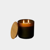 Los Poblanos Vela del Bosque Candle with dark frosted glass vessel, bamboo lid, and double wick candle burning