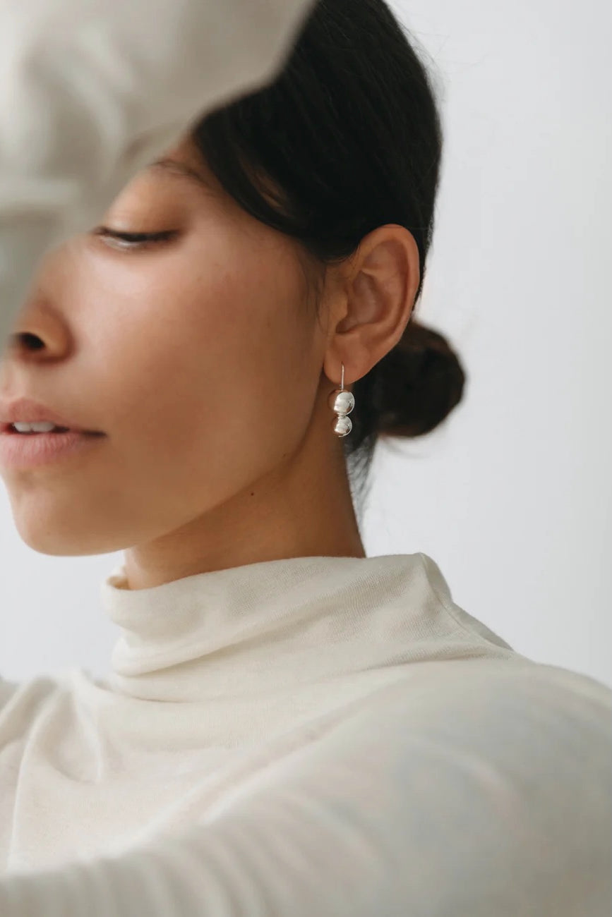 Maslo Jewelry double orb sterling silver drop earrings worn on model with neutral top, close-up side profile