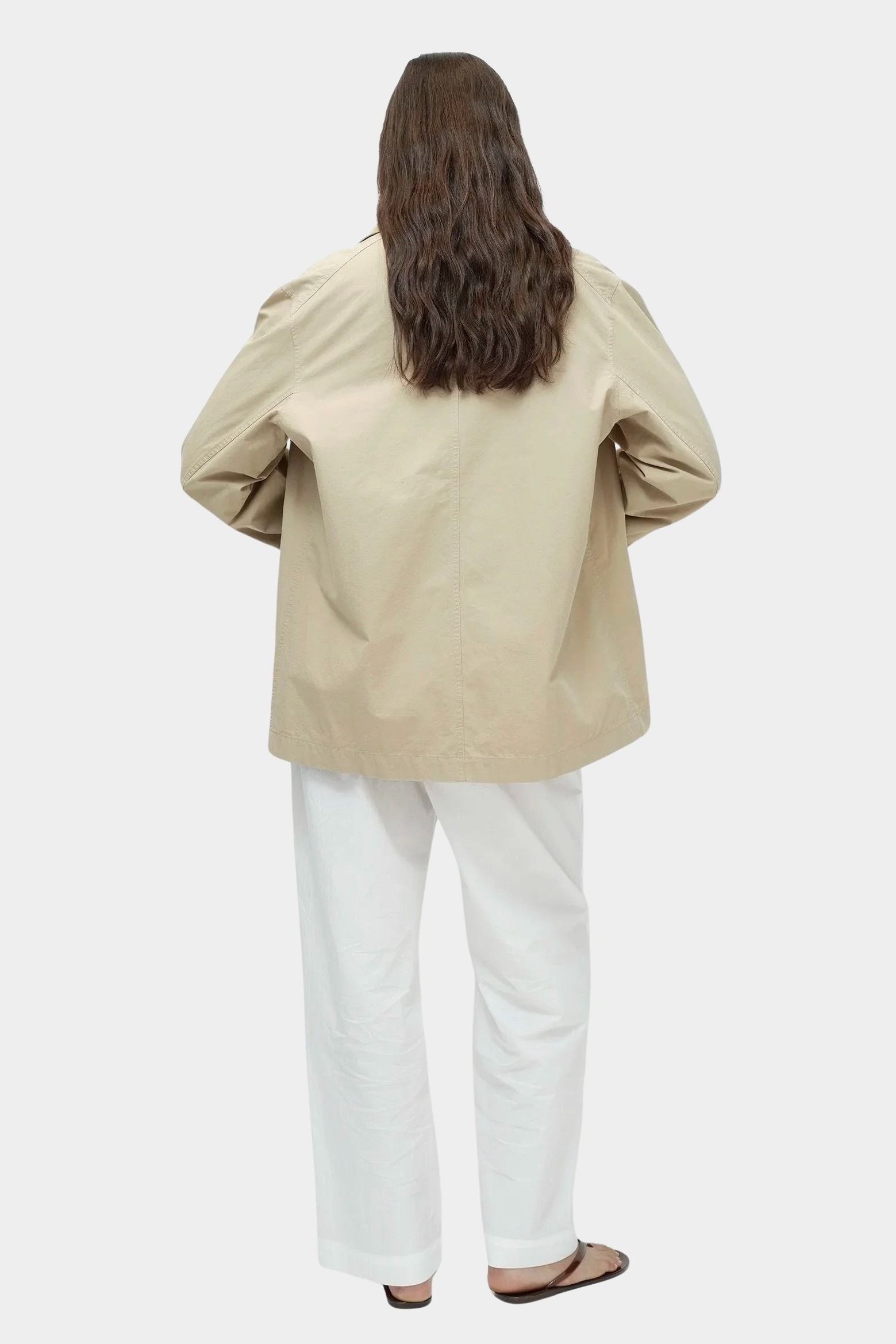 Back angled view of beige linen blend work jacket by Mijeong Park showing relaxed oversized fit