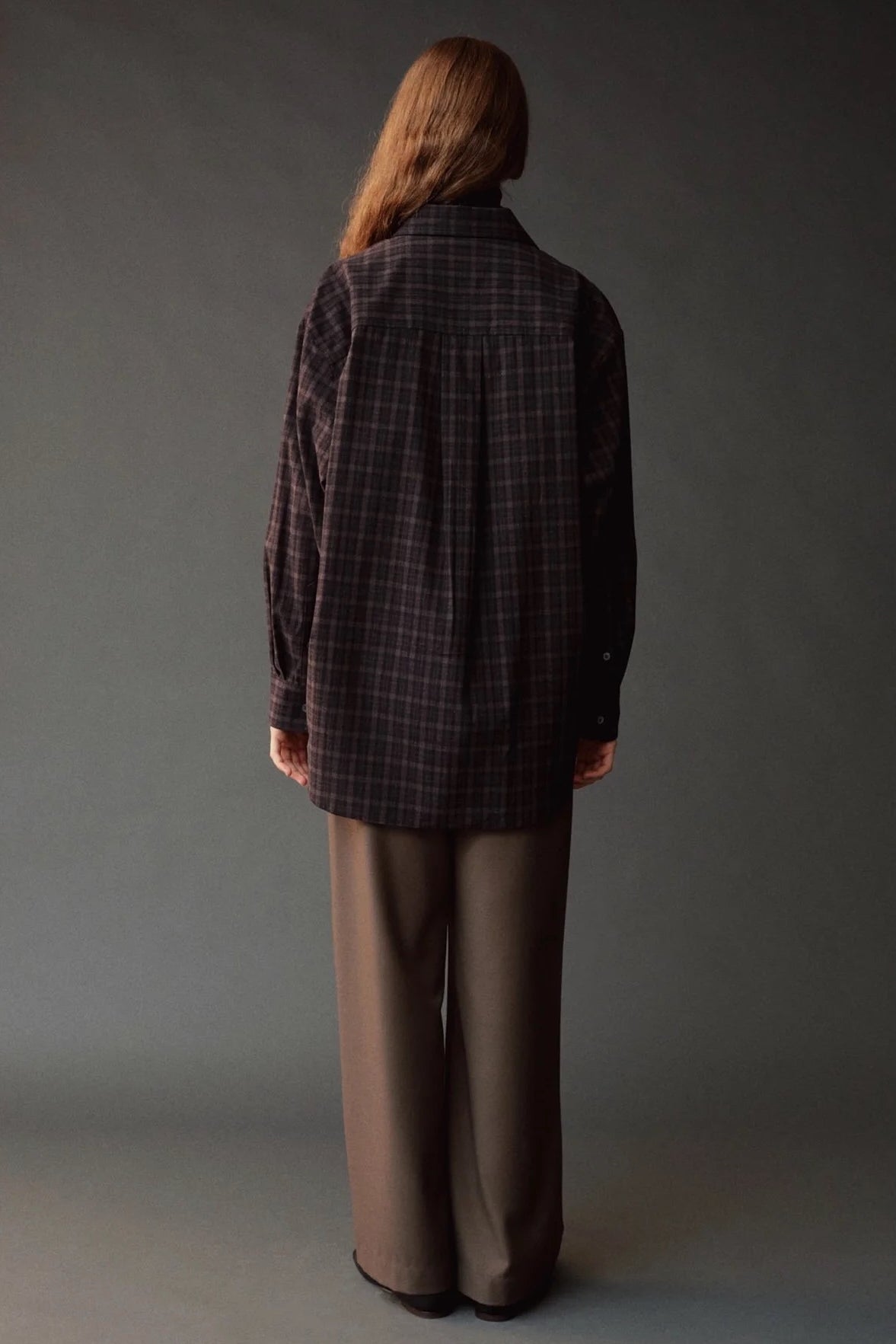 Back view of the Mijeong Park Oversized Plaid Shirt in black plaid showing the center pleat and curved hem
