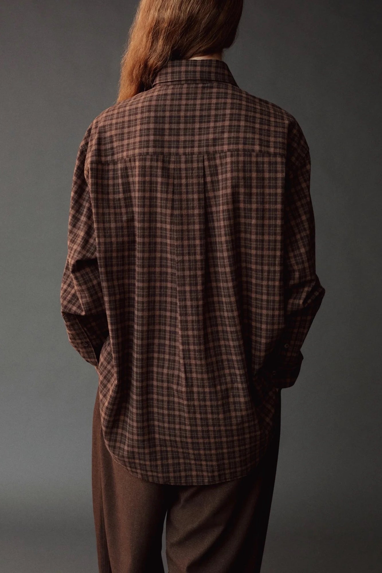 Close back view of the Mijeong Park Oversized Plaid Shirt showing the center pleat and curved hem