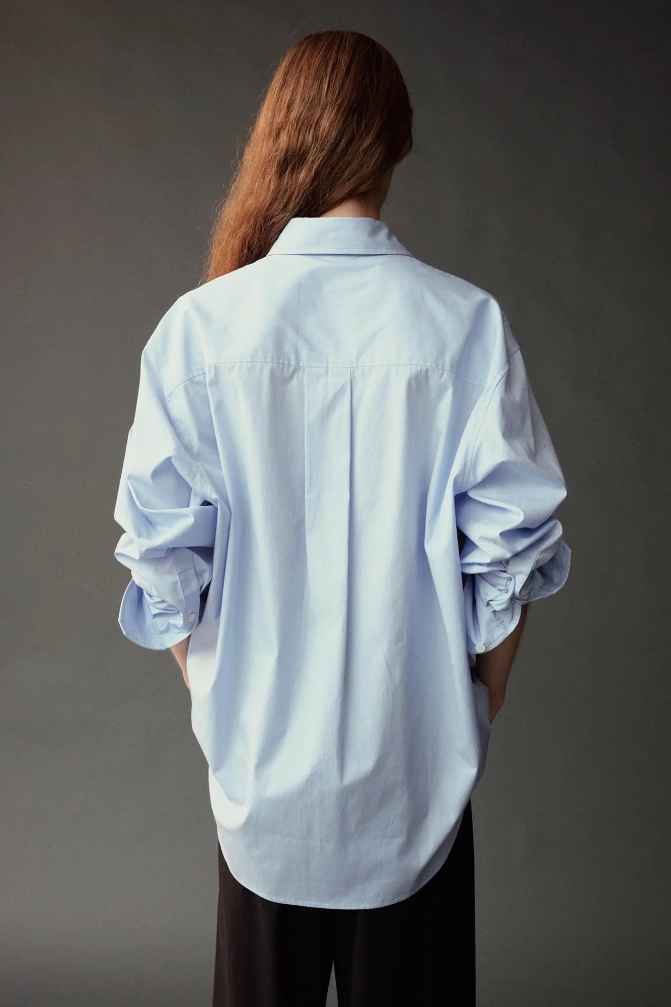 Back view of the Mijeong Park Oversized Shirt in light blue with rolled sleeves and a curved hem