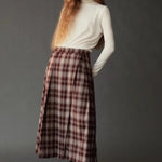 Model wearing the Mijeong Park brown plaid midi skirt with front pleats and an ivory turtleneck