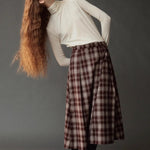 Model leaning to the side in the Mijeong Park brown plaid midi skirt and ivory turtleneck