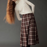Model leaning to the side in the Mijeong Park brown plaid midi skirt and ivory turtleneck
