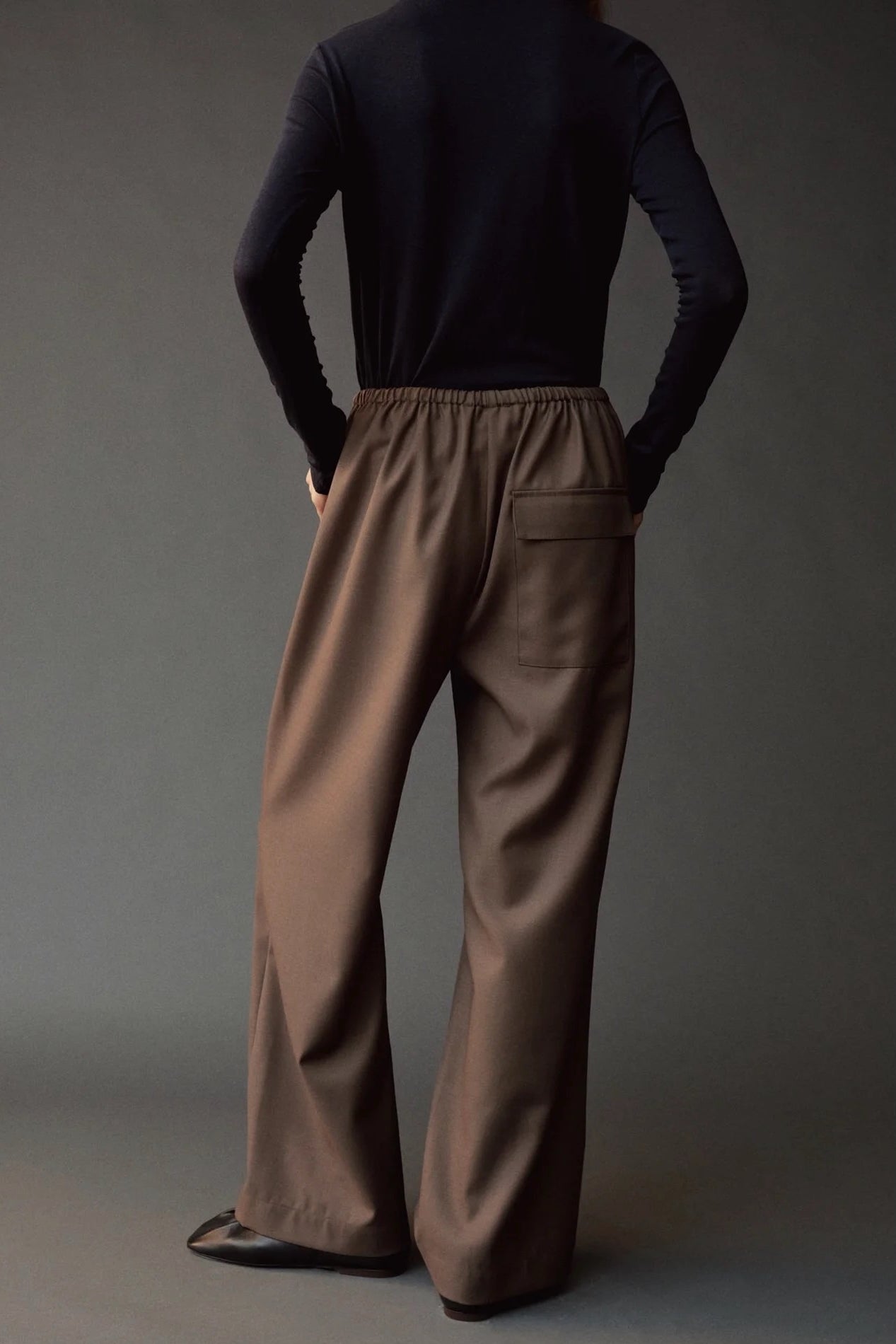 Back view of the dark navy roll neck jersey top styled with wide leg brown pants.