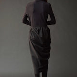 Graphite roll neck jersey top styled with a draped charcoal skirt and tights.
