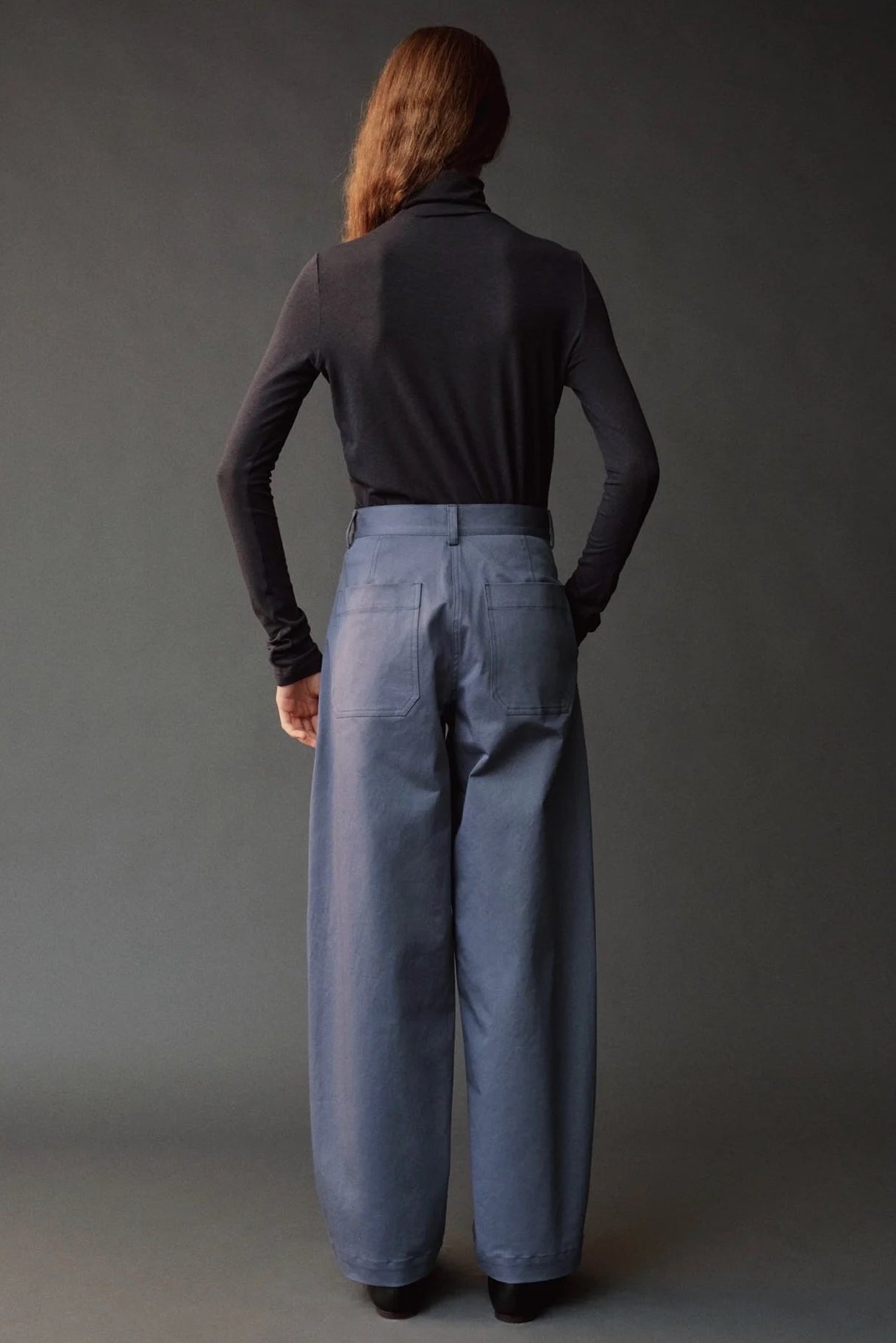 Back view of the graphite roll neck jersey top styled with blue wide leg pants.