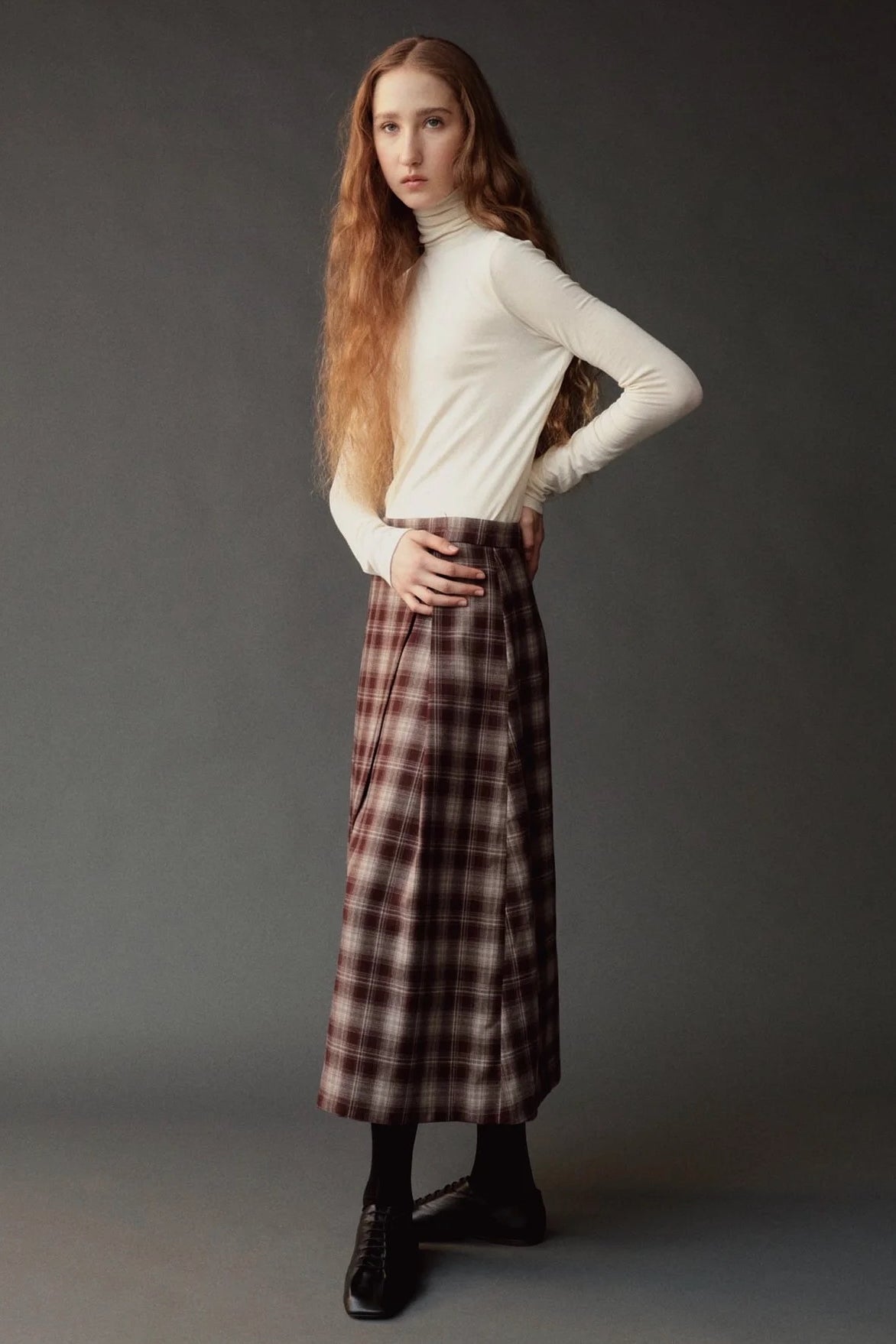 Side view of the ivory roll neck jersey top styled with a plaid midi skirt.