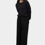 Side view of semi sheer black linen blend knit top by Mijeong Park styled with relaxed black trousers