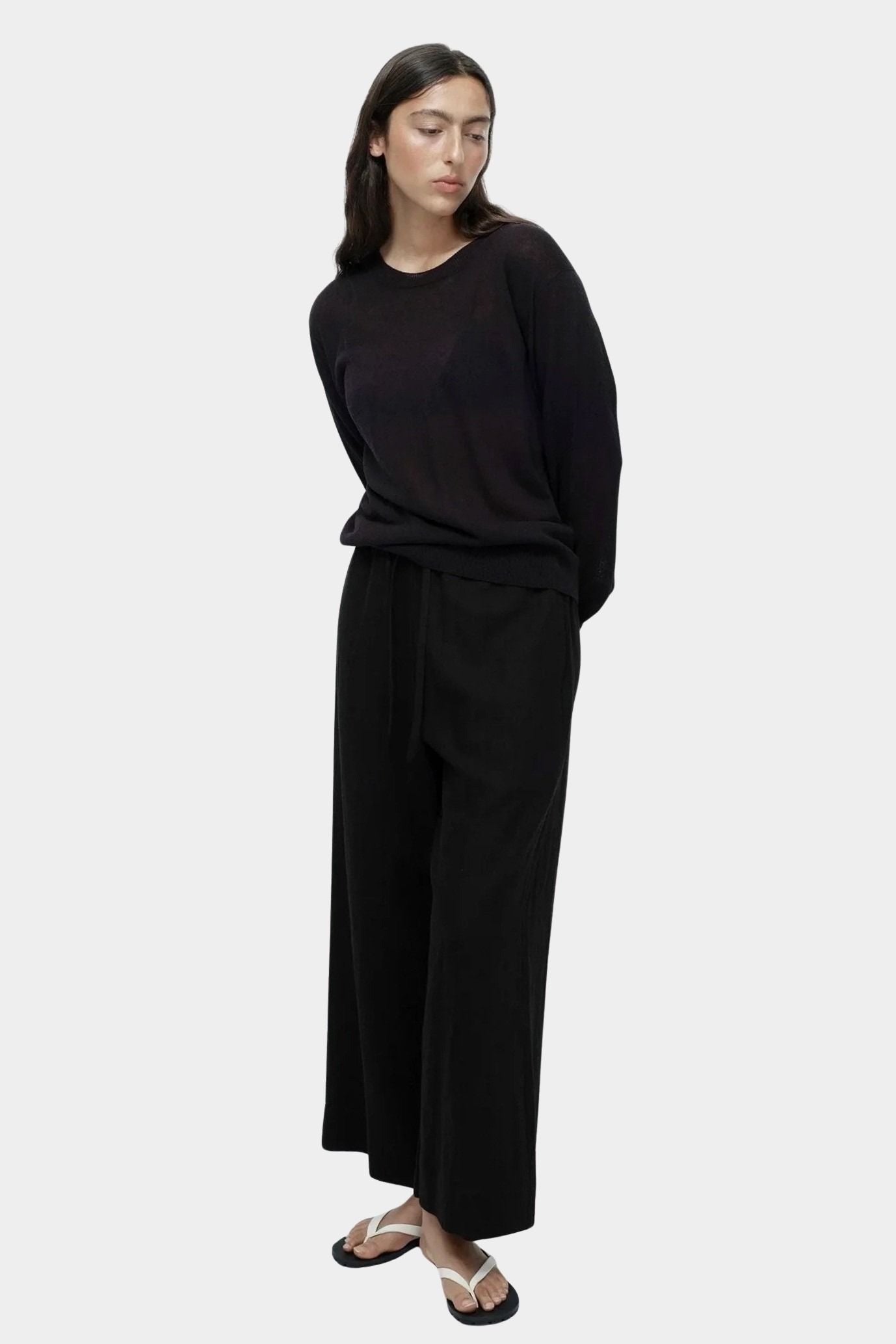 Side view of semi sheer black linen blend knit top by Mijeong Park styled with relaxed black trousers