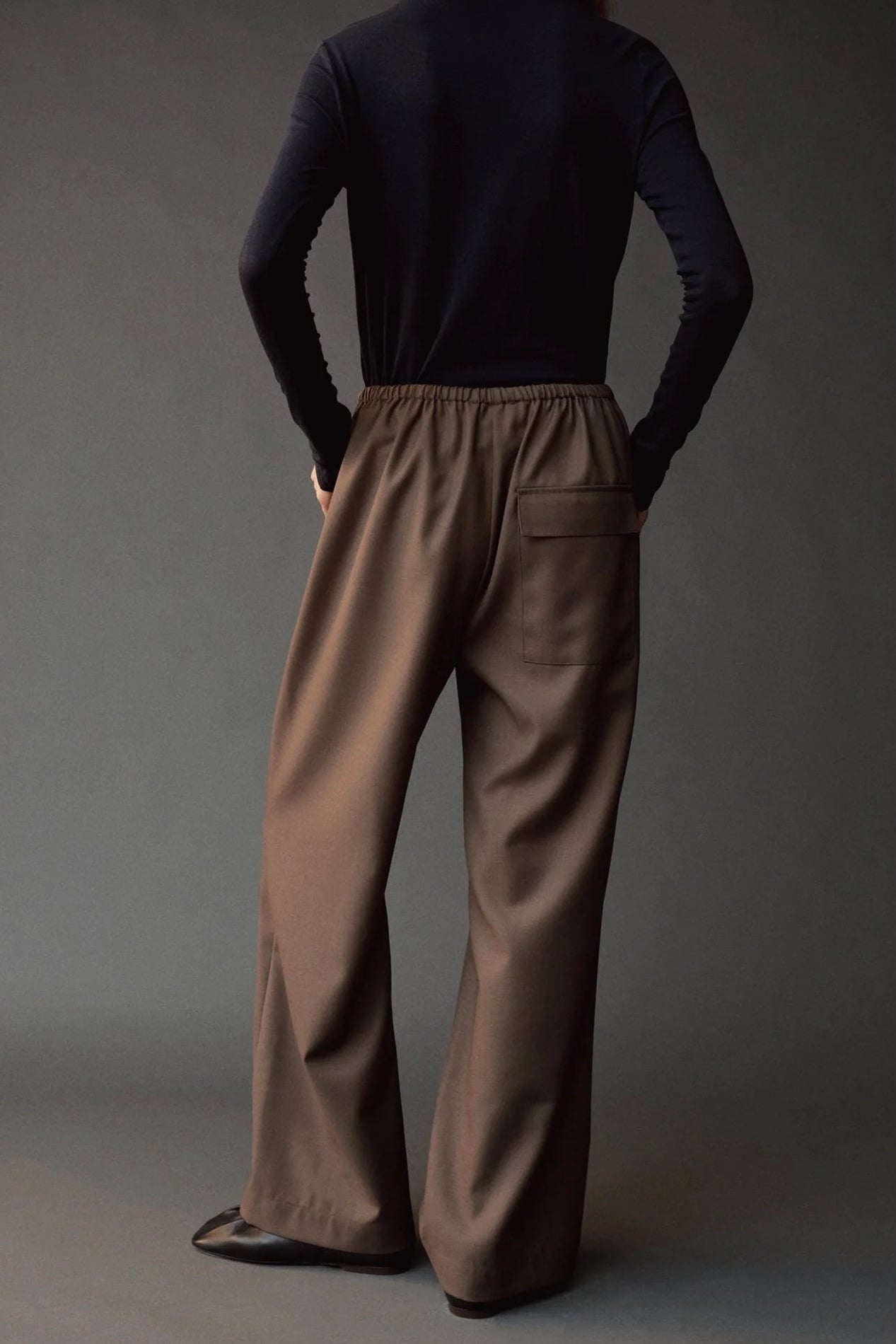 Close back view of the Mijeong Park olive brown pants showing the elastic waist and flap pocket