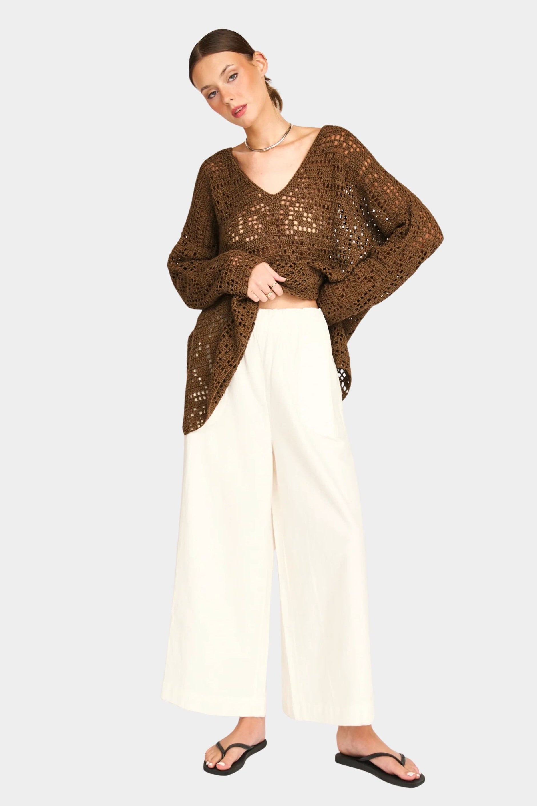 Full outfit view of white wide leg pants styled with oversized brown sweater and sandals