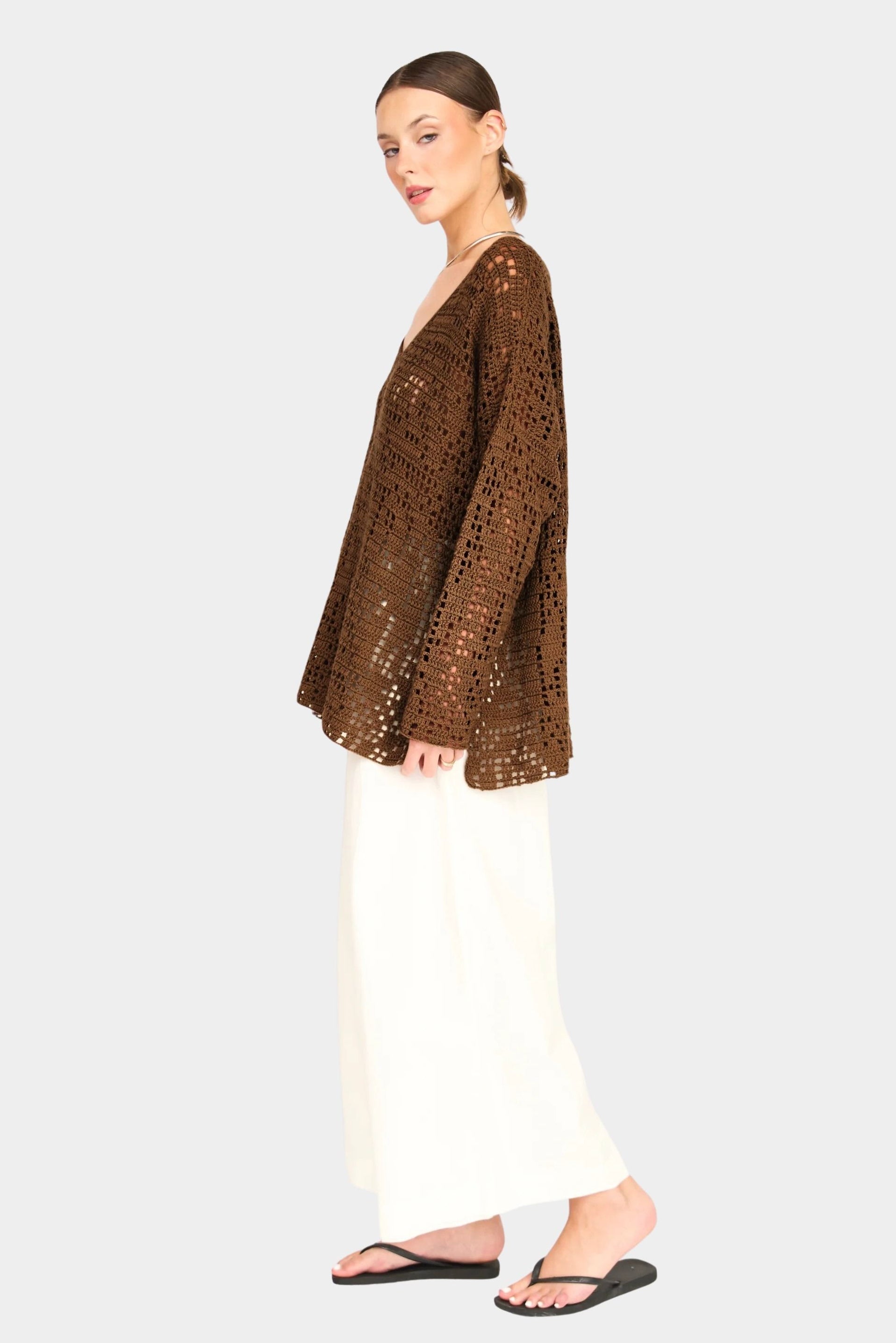 Side view of white wide leg pants styled with brown knit top, relaxed fit and ankle length silhouette