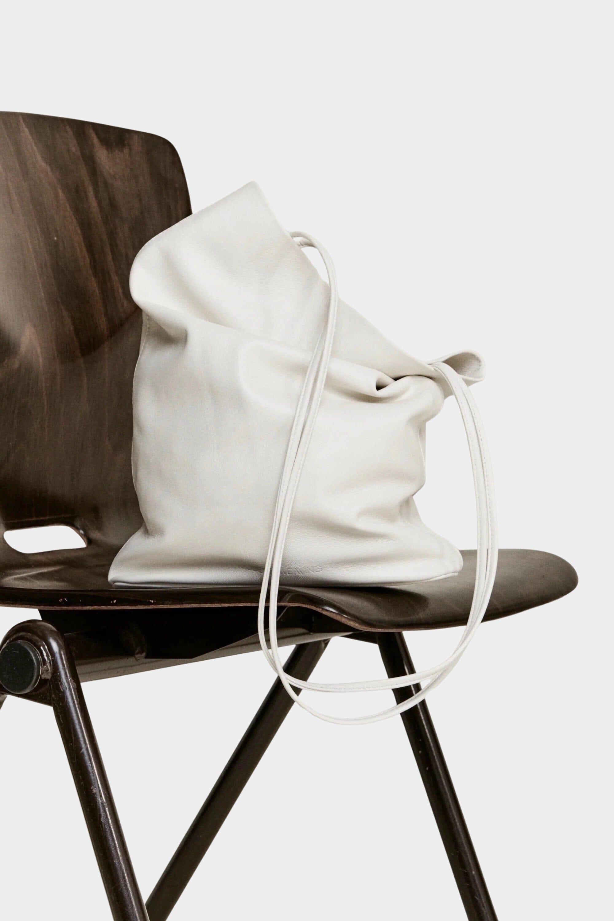 Modern Weaving Slim Elongated Tote Creme in Italian lamb leather draped over wooden chair with soft structure and long shoulder straps