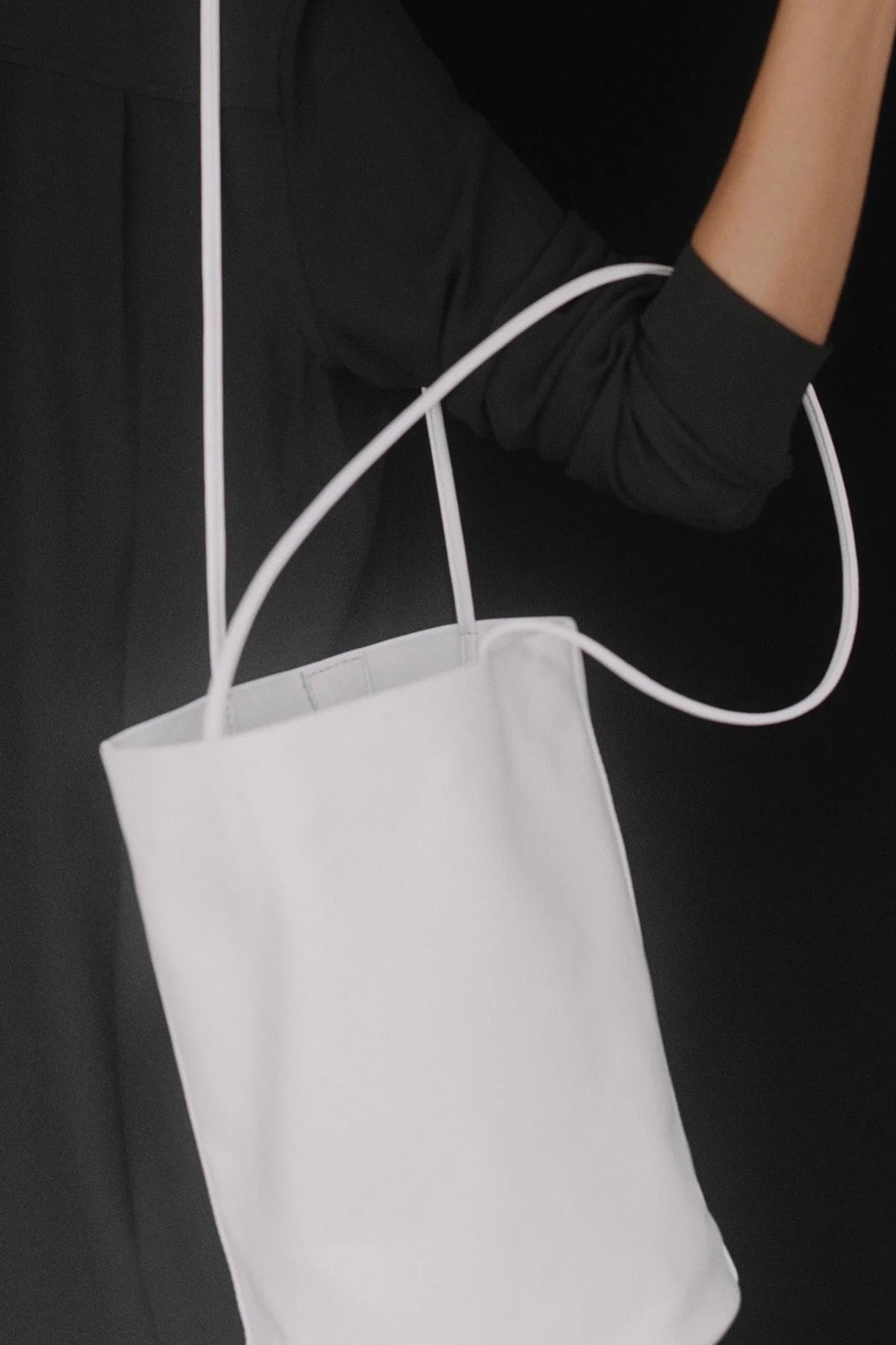 Modern Weaving Drape Oval Bucket in Creme carried by its slender straps against a black outfit