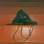 Slim Lamb Sak in Braun resting on an orange bench with its leather folded and straps hanging forward