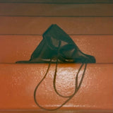 Slim Lamb Sak in Braun resting on an orange bench with its leather folded and straps hanging forward