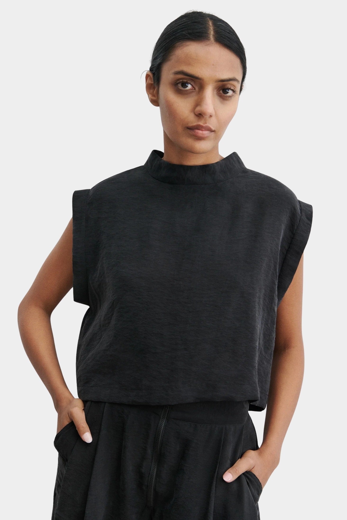 Rachel Comey Bacchus top in black with sculptural sleeveless design, structured mock neckline, and boxy cropped silhouette, styled with matching trousers