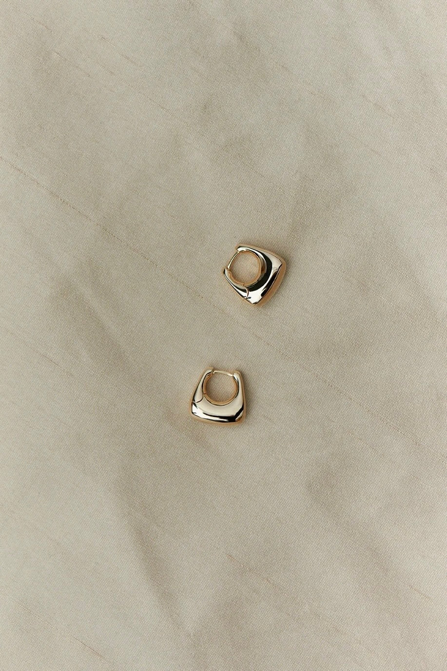 Sculptural RAGBAG Studio gold plated sterling silver Datura earrings arranged on natural textured fabric