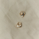 Sculptural RAGBAG Studio gold plated sterling silver Datura earrings arranged on natural textured fabric