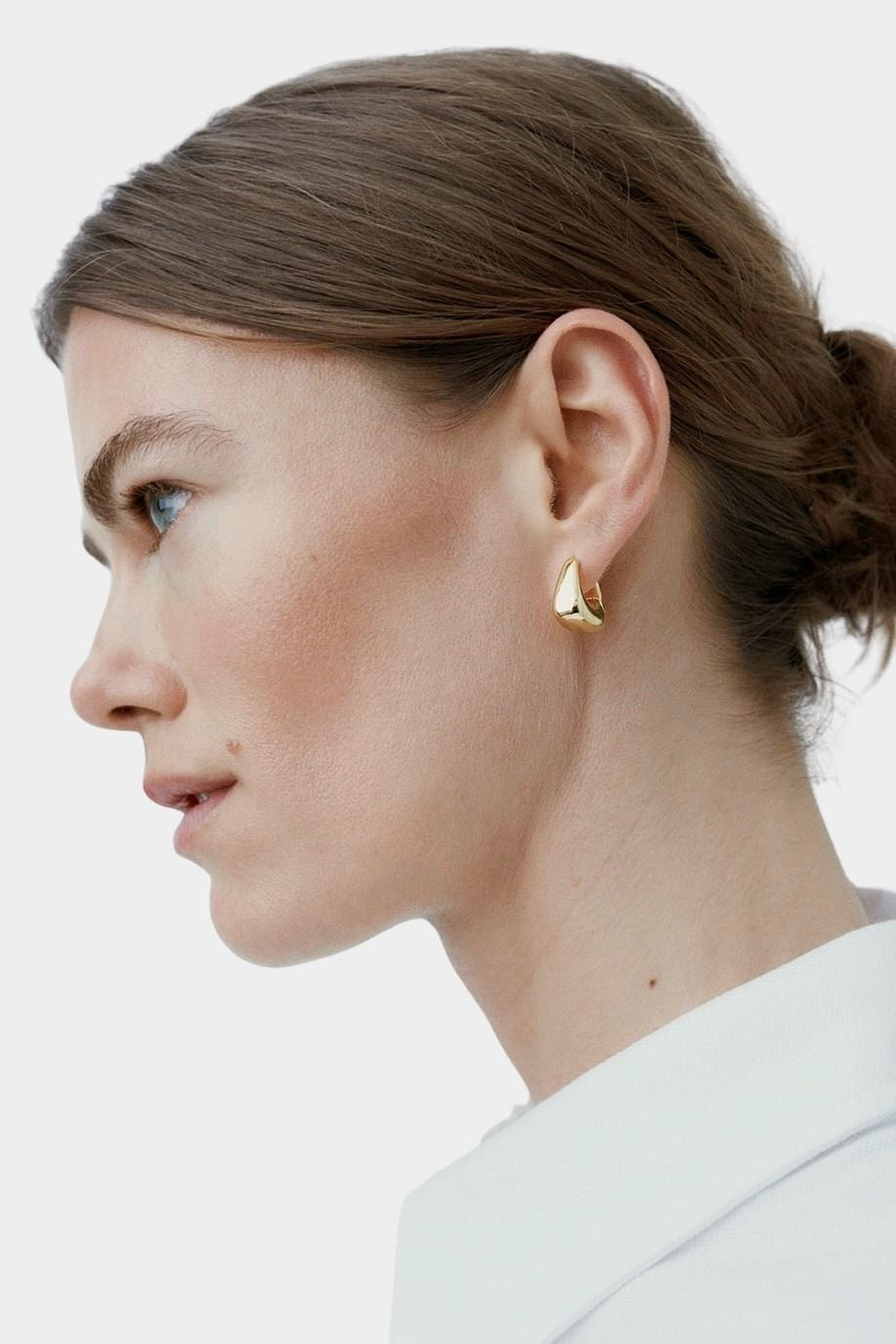 RAGBAG Studio Datura gold hoop earring worn on model in side profile, showing sculptural shape