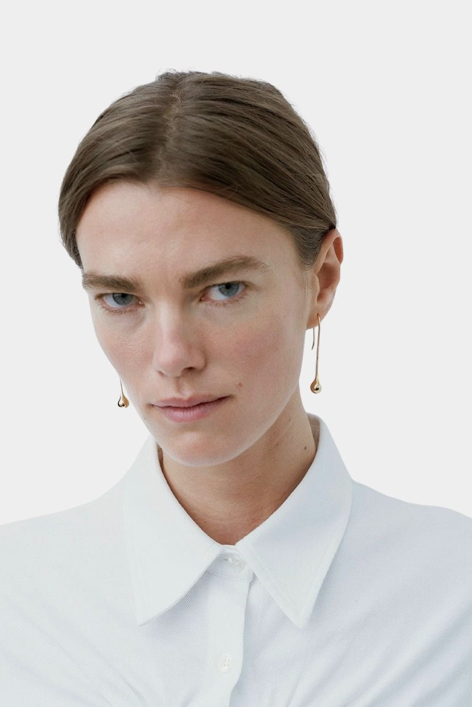 Model wearing long gold droplet earrings by RAGBAG Studio with a white collared shirt